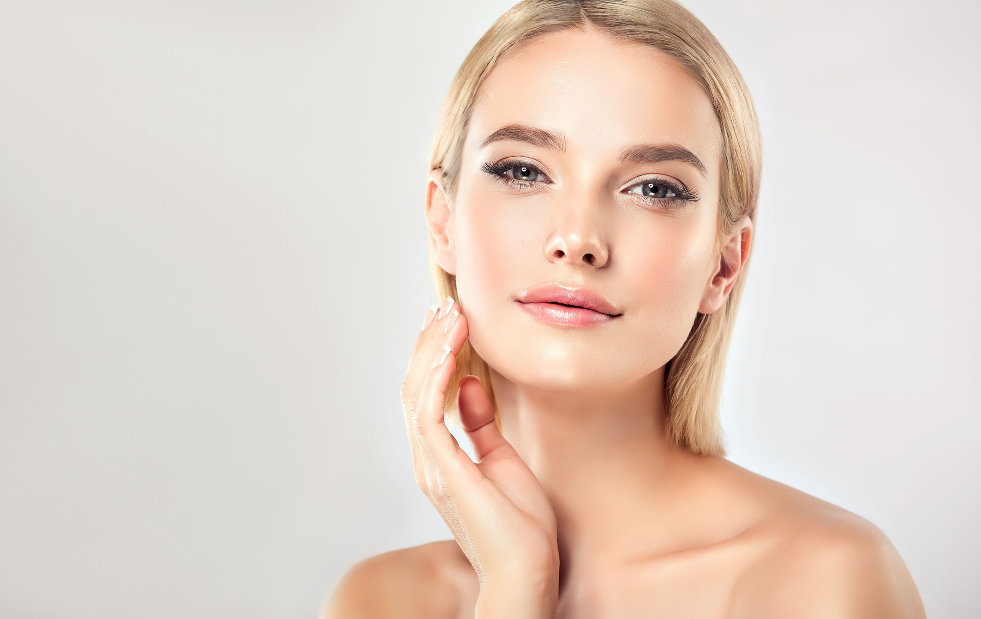 Wunderschön, jung, Frau mit Mandel-ähnlichen Augen berührt zärtlich das Gesicht. Gesichtsbehandlung, Kosmetologie und Spa.